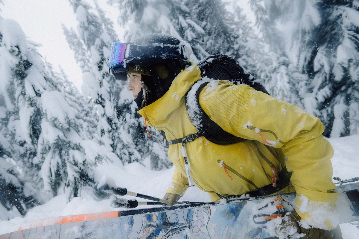 A skier in a yellow jacket and goggles among snow-loaded trees