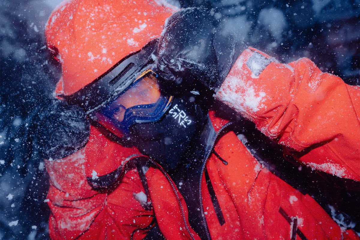 A skier in a red jacket and goggles, wearing a STRATUS balaclava in falling snow