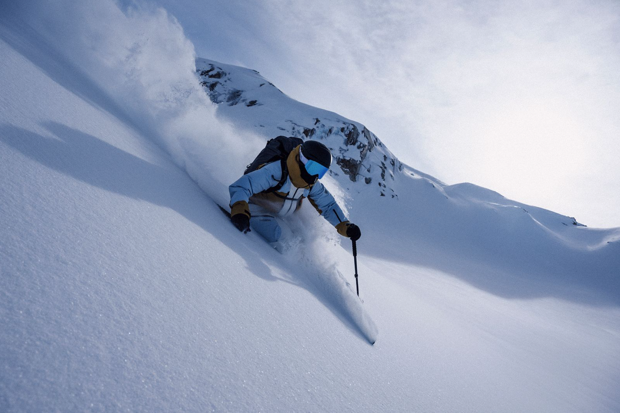 Person skiing down a snowy mountain with a blue sky above