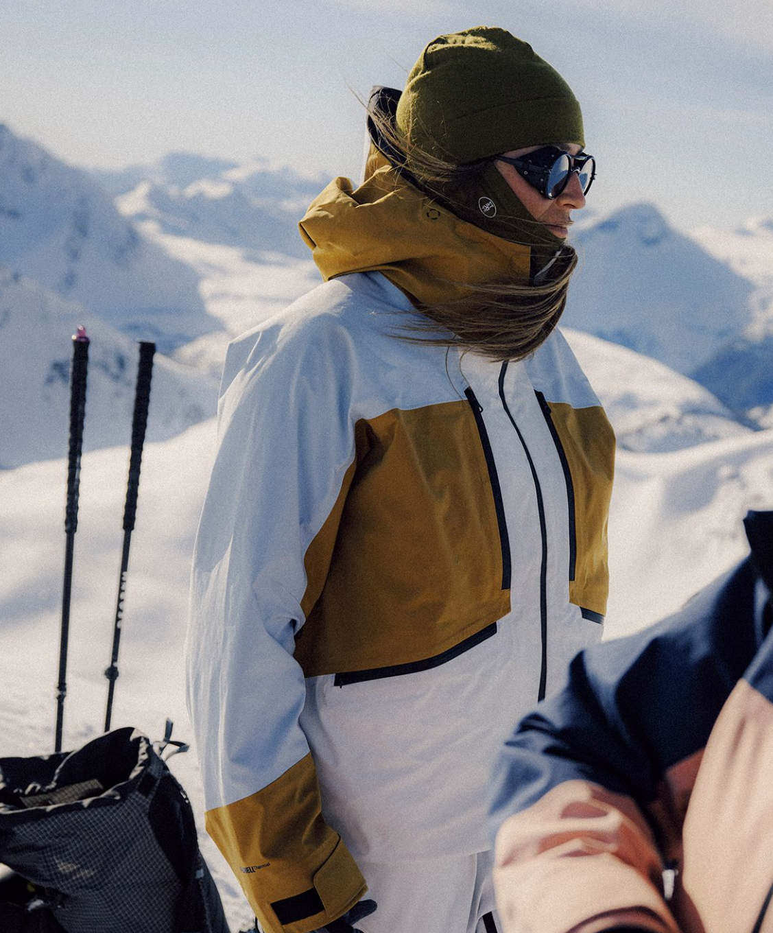 Two people in winter gear standing on a snowy mountain with skis and backpacks.