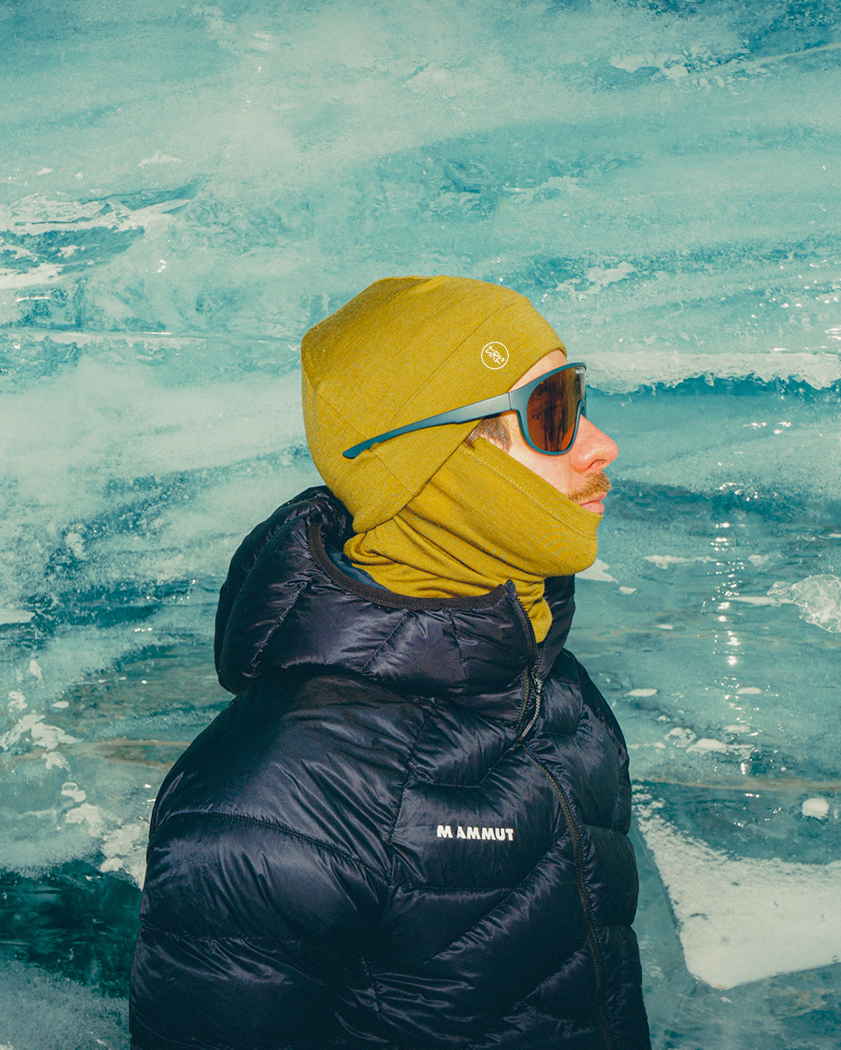 Person wearing a merino beanie and neck warmer and black jacket in front of ice formations