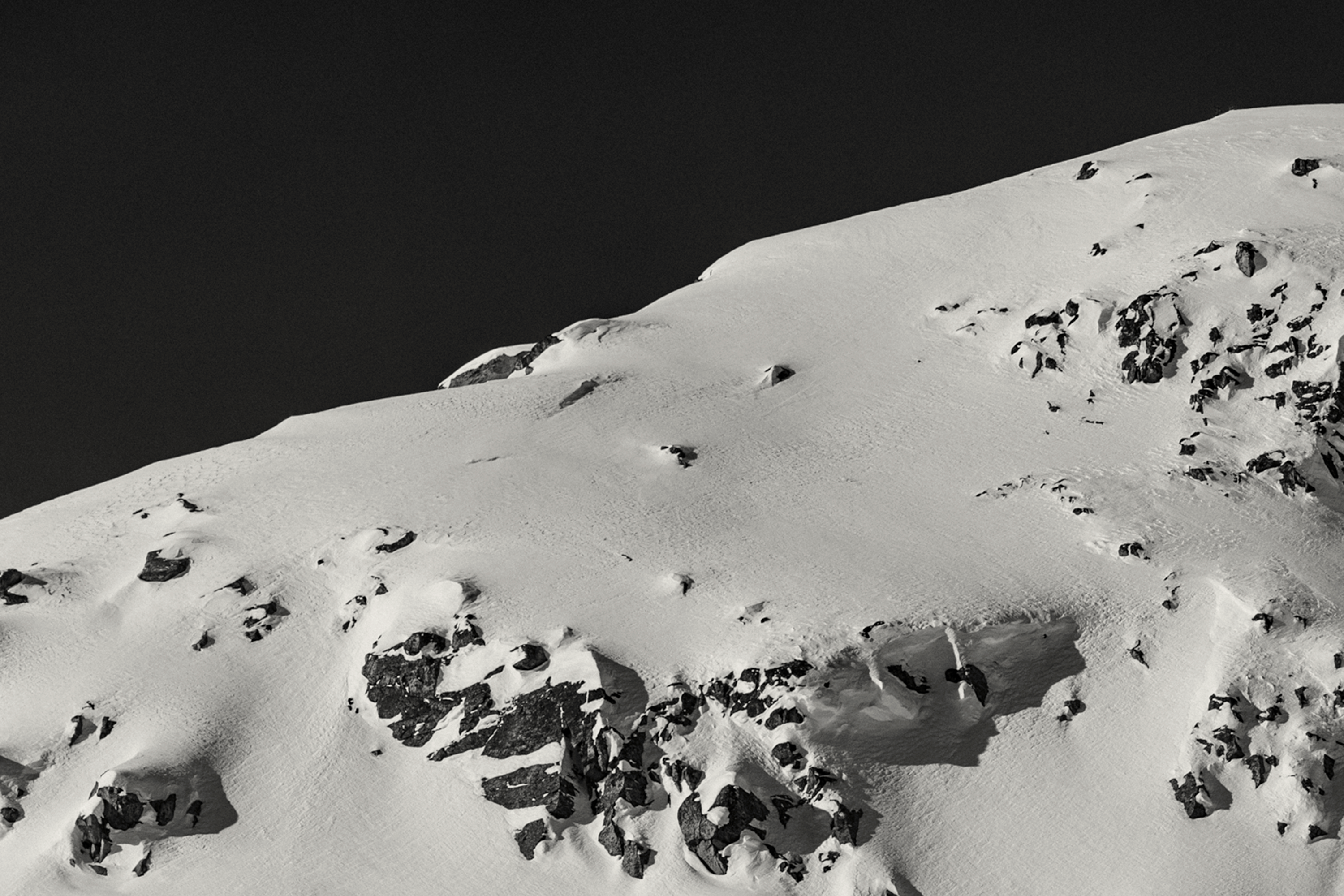 Snow-covered mountain with rocky outcrops against a dark sky