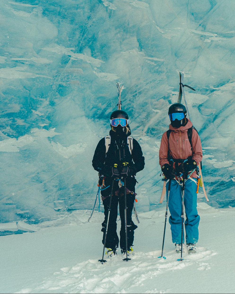 Two people with ice axes and helmets standing on a glacier with a large ice wall in the background.