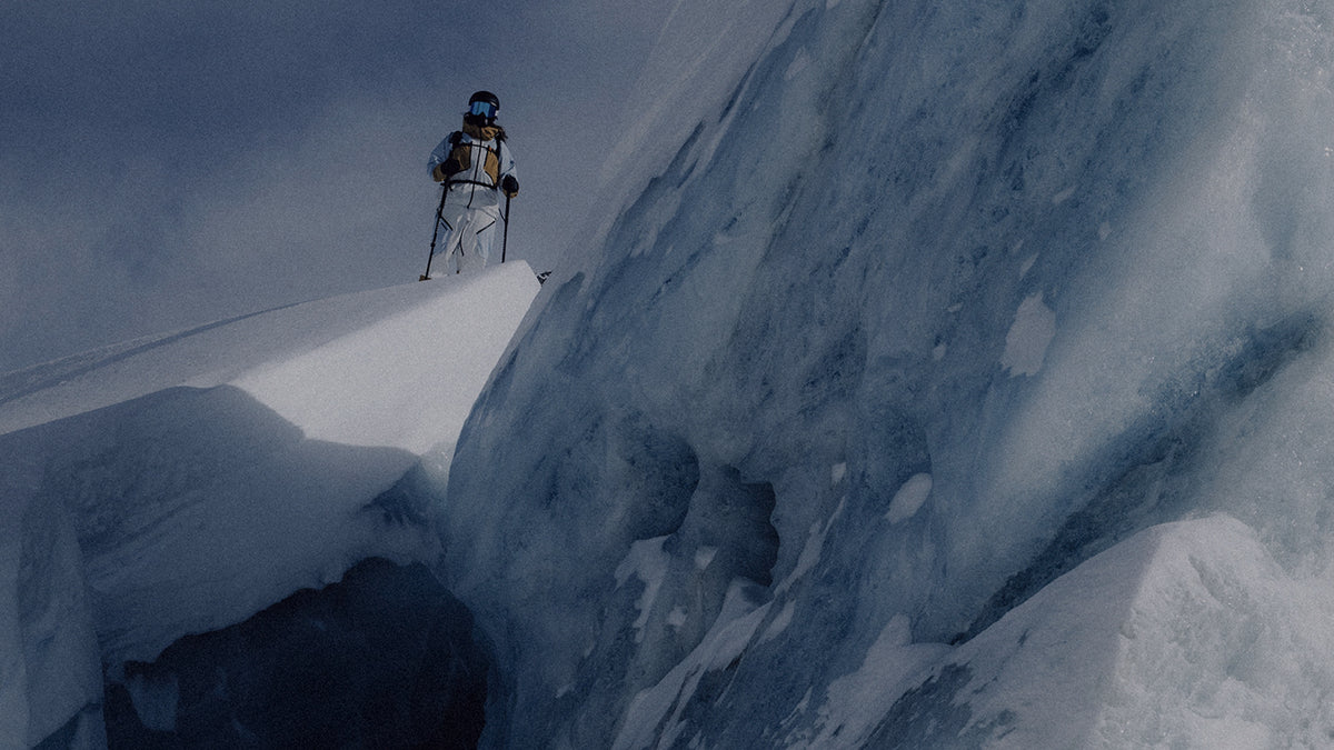 A skier on a snow cornice above a wall of blue ice
