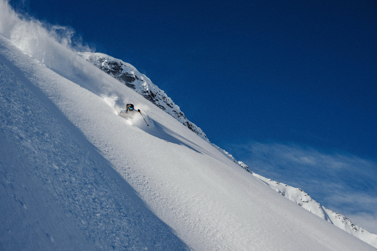 A skier descends a steep powder slope under a deep blue sky