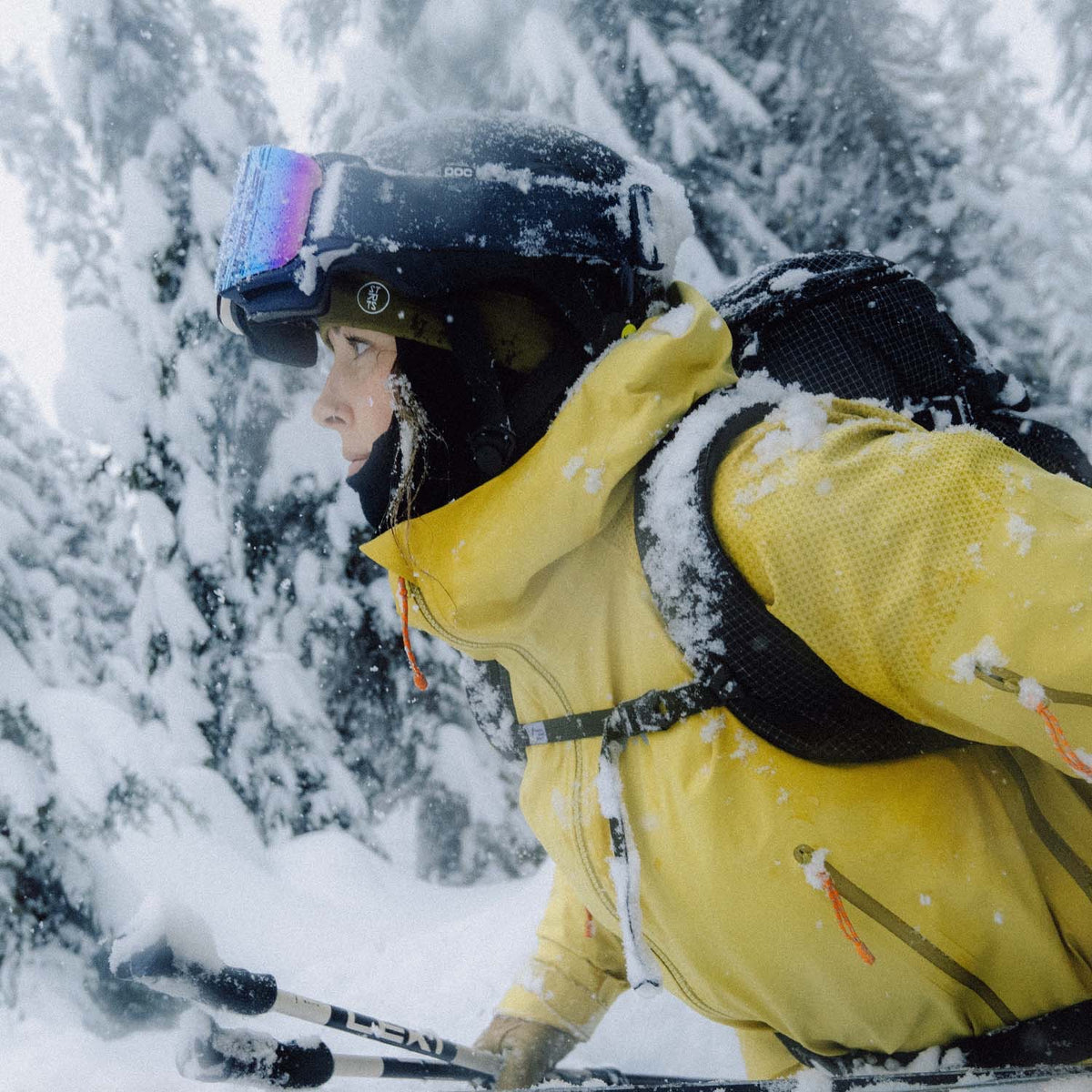 A skier in a yellow jacket and goggles in falling snow